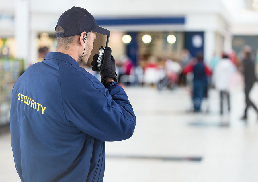 Digital composite of back of security guard with walkie talkie against blurry shopping center