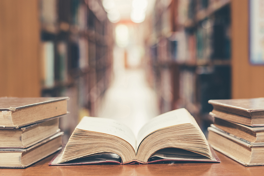 Old book in library with open textbook stack piles of literature text archive on reading desk